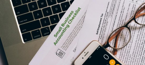 Small business accounting setup featuring a laptop, documents, and smartphone calculator.
